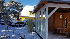 A wooden cabin with a covered porch, surrounded by snow-covered trees and a clear blue sky. - Fewo 4 Triftweg 10 (Loddin)