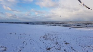 A snowy beach with footprints leading to the water, a clear sky, and a distant lighthouse. - Fewo 4 Triftweg 10 (Loddin)