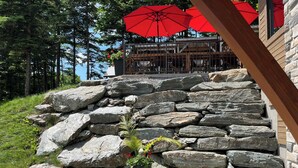 Eine Steintreppe führt zu einer Holzhütte mit roten Sonnenschirmen.