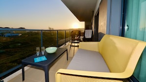 A balcony with a sofa, a table with two glasses and a bowl, and a view of the sunset over a landscape.