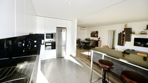 A modern kitchen with stainless steel appliances, a bar area with stools, and a dining area with a wooden table and chairs.