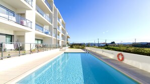 A swimming pool adjacent to a multi-story building with balconies, a lifebuoy, and a clear sky.