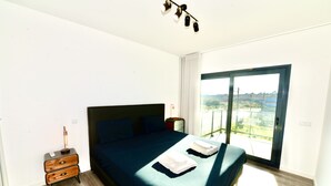 A bedroom with a large bed, a nightstand, and a view of the outdoors through a sliding glass door.