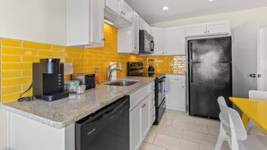 A compact kitchen with white cabinets, a black refrigerator, a microwave, a coffee maker, and a sink. - TreeHouse Lodge*Walk to Beach*Pet-Friendly (#106) (North Myrtle Beach)