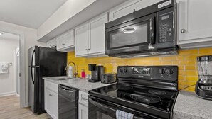 Una cocina moderna con armarios blancos, un refrigerador negro, un microondas, una estufa y una cafetera.