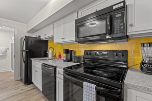 A modern kitchen with white cabinets, a black refrigerator, a microwave, a stove, and a coffee maker.
