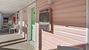 Un pasillo con un dispensador de agua en la pared, una puerta verde y sillas blancas a lo largo del lateral.