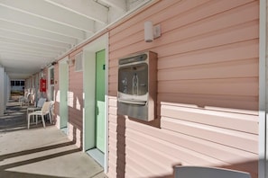 A corridor with a water dispenser mounted on the wall, a green door, and white chairs along the side.