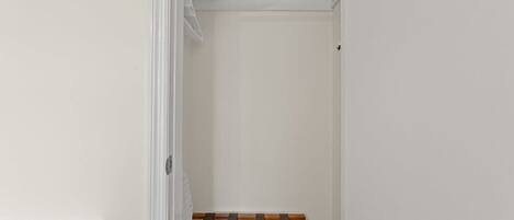 A narrow walk-in closet with a wooden drying rack and neatly folded towels on a shelf.