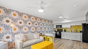 A modern living room with a sofa, yellow ottoman, and patterned wallpaper. - TreeHouse Lodge, Walk to Beach, Pet-Friendly 203 (North Myrtle Beach)