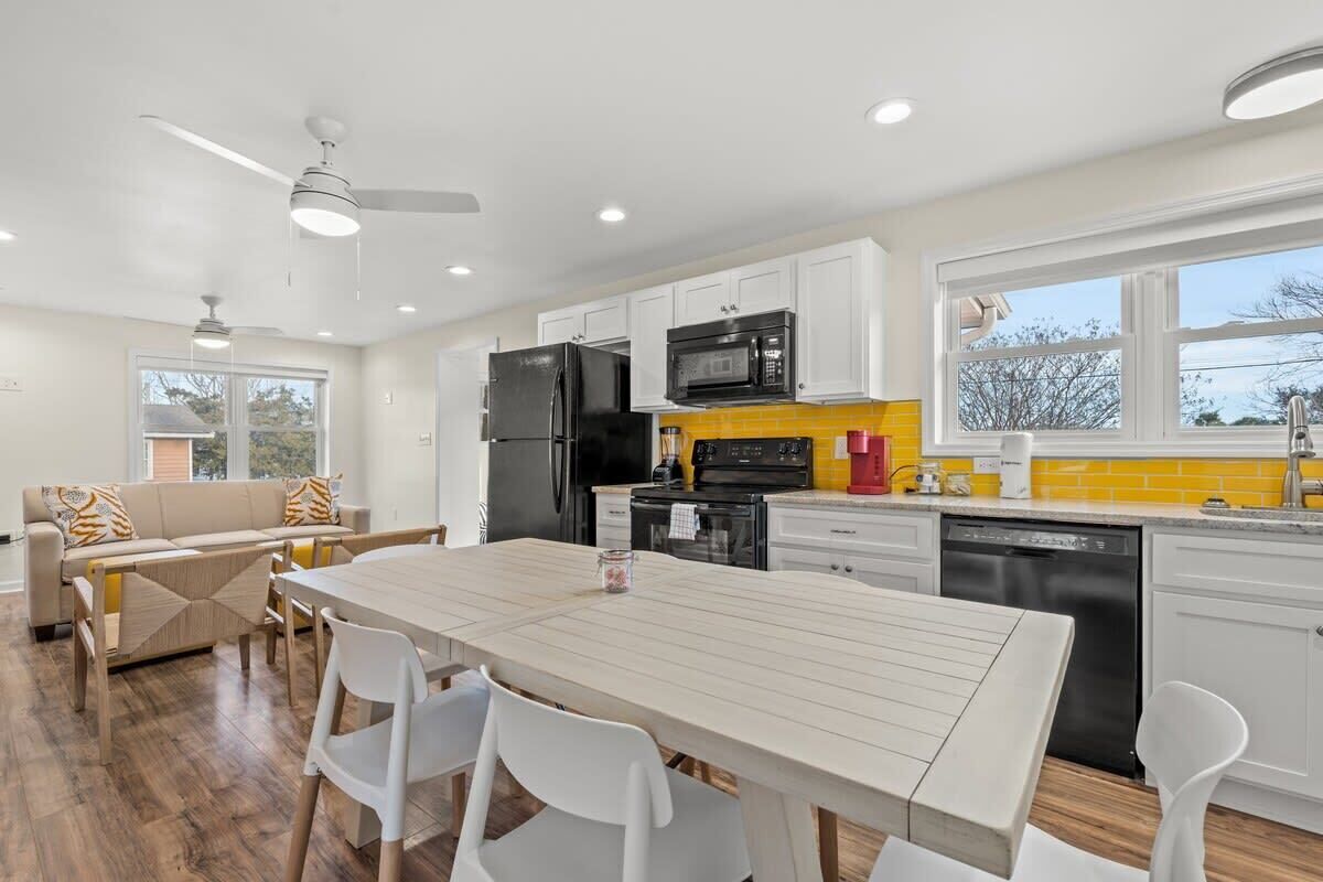 A modern kitchen with white cabinets, a black refrigerator, a microwave, and a dishwasher. There is a dining table with chairs in the center.
