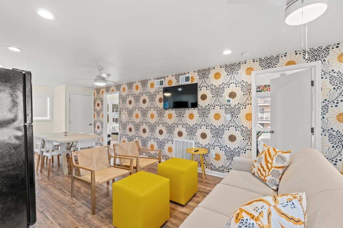 A modern living room with a sofa, yellow ottomans, and a TV mounted on the wall.