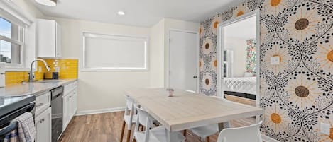 A compact kitchen with a wooden table and white chairs, a yellow backsplash, and a patterned wall.