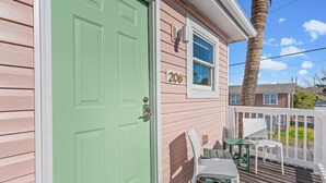 Una casa con puerta verde, el número '206' en la pared, y una terraza con sillas y una mesa.