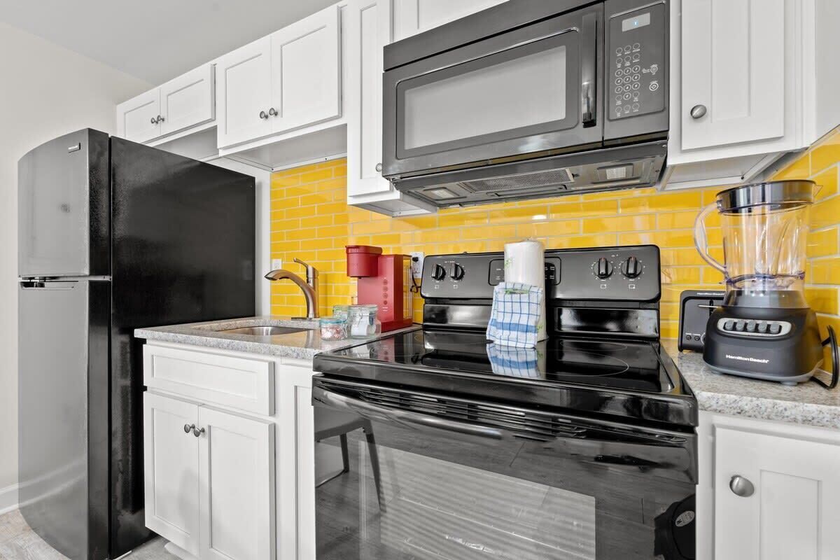 Una cocina moderna con gabinetes blancos, un refrigerador negro, un microondas, una estufa y una licuadora.