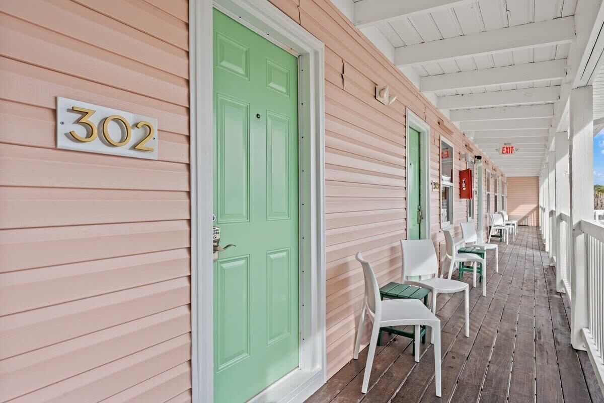 A porch with a green door, white chairs, and a sign indicating room number 302.