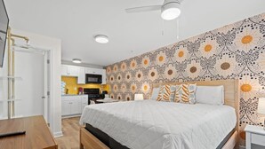 Ein Schlafzimmer mit Bett, Nachttisch und Blick auf die Küche im Hintergrund.