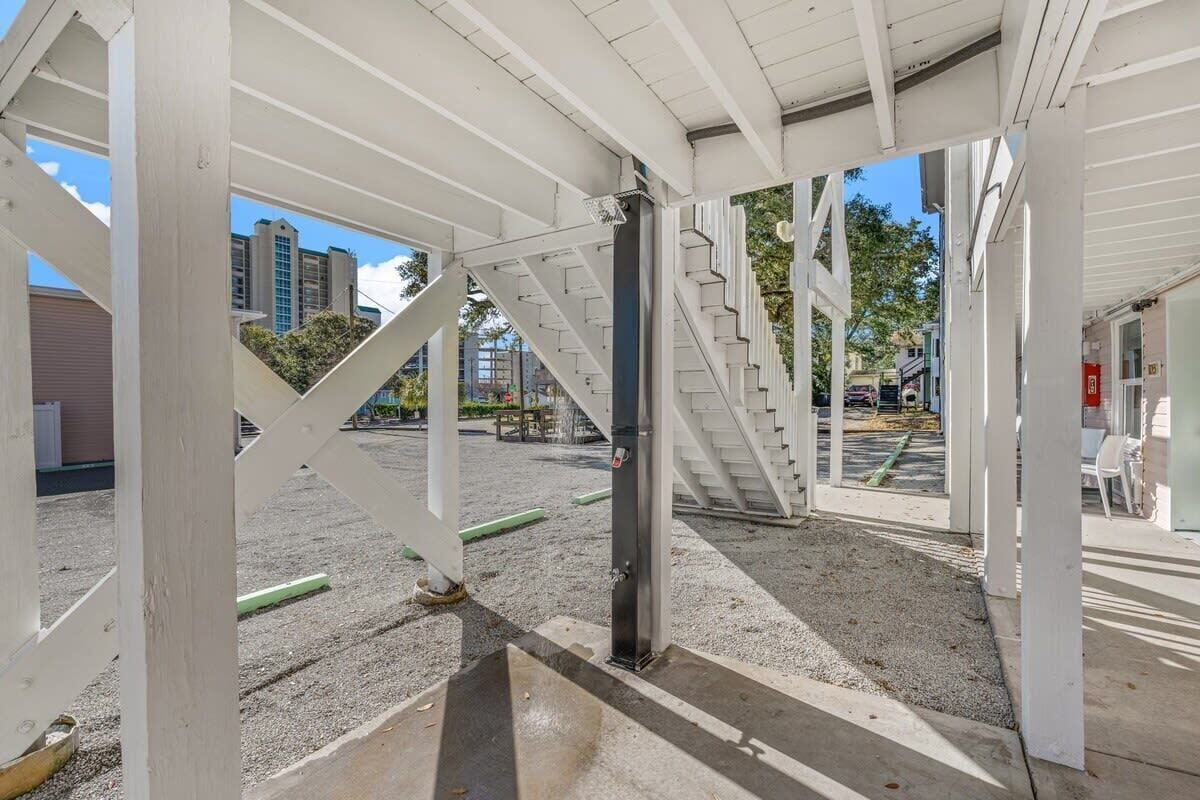 Un espace extérieur abrité, doté d’un escalier menant à un niveau supérieur et entouré d’éléments structurels blancs.