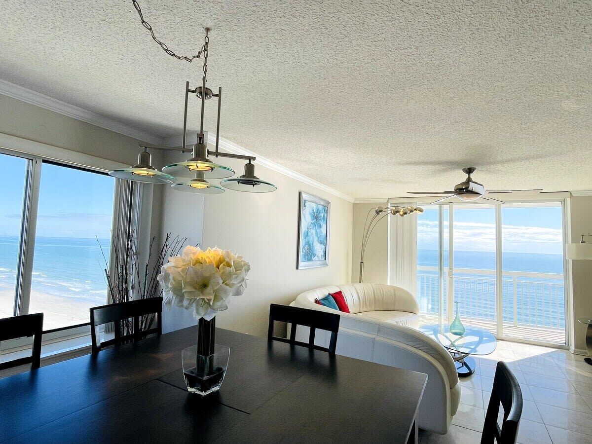 A dining area with a table, chairs, and a vase of flowers. There is a sofa with a view of the ocean.