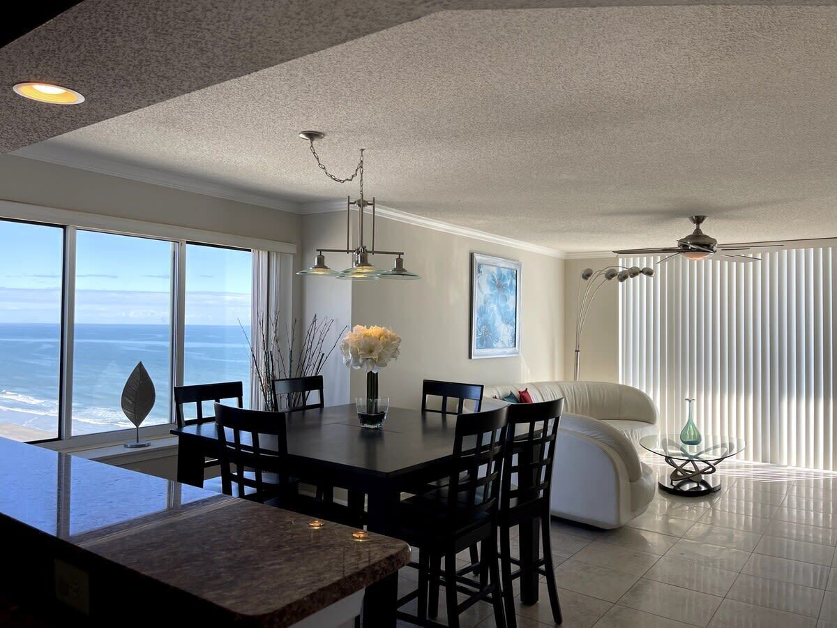 A modern dining area with a large table, chairs, and a view of the ocean.