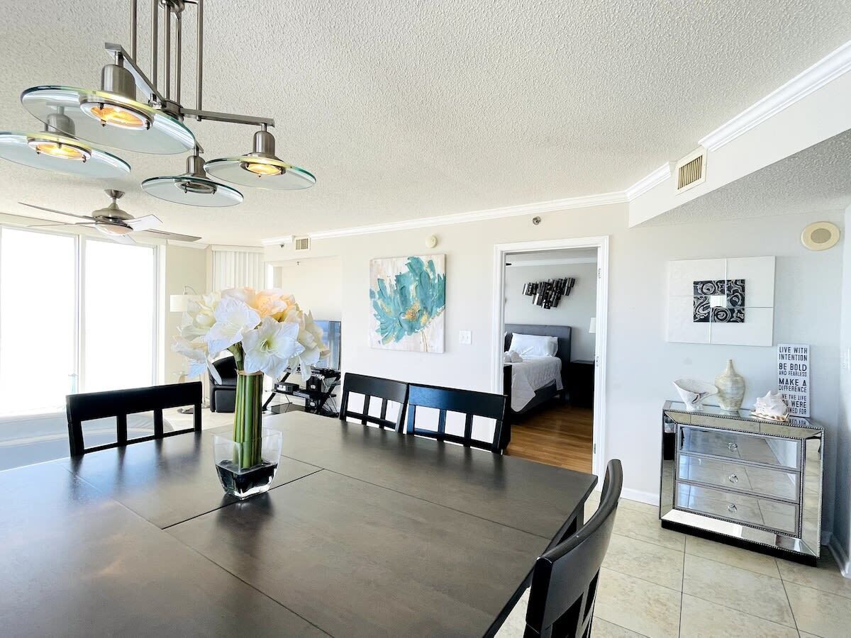 A modern dining room with a large table, chairs, a vase of flowers, and a ceiling fan.