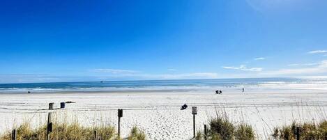 A beach with a wooden boardwalk leading to the shore, clear skies, and calm sea.