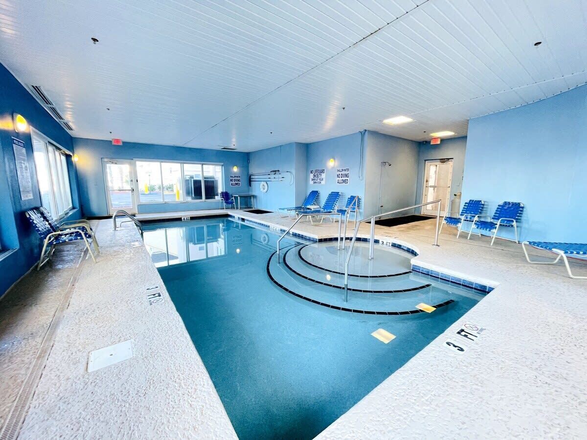 An indoor swimming pool with blue walls, a tiled floor, and blue chairs along the sides.