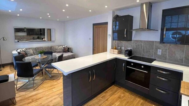 A modern kitchen with dark cabinets, a large island, and a built-in oven. - Modern City Center 2 Bedroom Apartment (Aberdeen)
