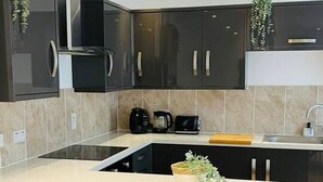 A modern kitchen with dark cabinetry, a central island, and a built-in oven. - Modern City Center 2 Bedroom Apartment (Aberdeen)