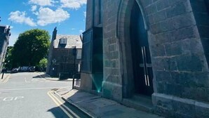 A street view with a building featuring a large arched entrance and a clear blue sky with the sun shining. - Modern City Center 2 Bedroom Apartment (Aberdeen)