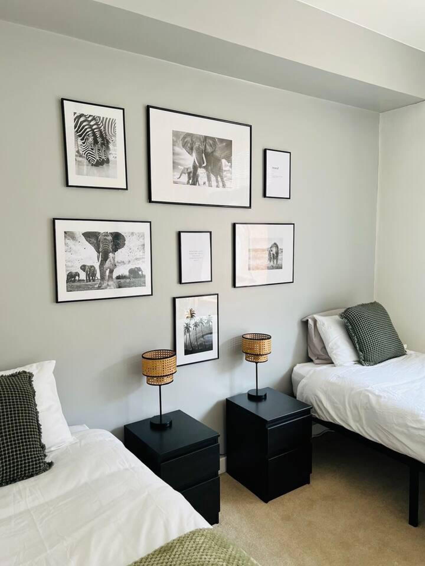 Une chambre avec deux lits, une étagère murale ornée de tableaux encadrés et deux tables de chevet avec des lampes.