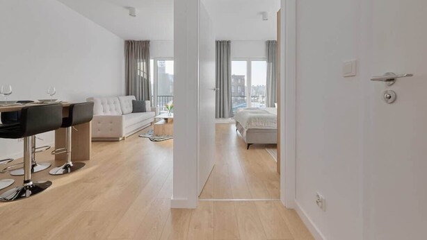 A modern hotel room with a dining area, a sofa, a bed, and a view of the city. - Modern Apartment | Parking, Balcony, Workspace (Wroclaw)
