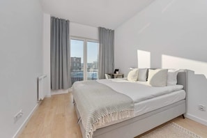 A modern bedroom with a large bed, a view of the city, and a small desk.