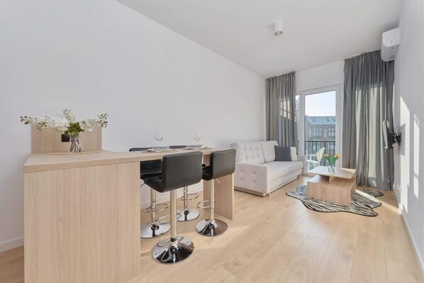 A modern living room with a sofa, a coffee table, and a dining area with a bar.