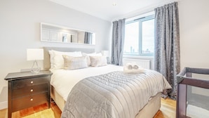 A hotel room with a bed, a nightstand, a window with curtains, a view of the city, and a crib.