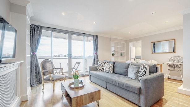 A modern living room with a grey sofa, wooden coffee table, and a view through large windows.
