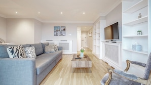 A modern living room with a grey sofa, a coffee table, and a TV on a white stand.