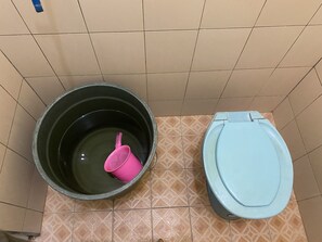Een badkamer met een toilet en een grote emmer vol water.
