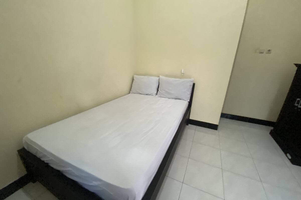Une petite chambre avec un lit simple, une literie blanche, une tête de lit noire et un sol carrelé.