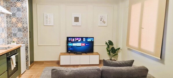 Una sala de estar con una televisión de pantalla plana sobre un soporte de madera, un sofá gris y una planta en maceta.