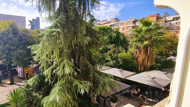 A courtyard with a large tree, outdoor seating, and a view of residential buildings.