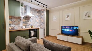 A compact living space with a kitchenette, a flat-screen TV, a sofa, and a potted plant.