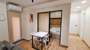 A compact living space with a dining table, a sofa, a bed, and a sliding door leading to a bedroom.