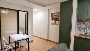 A small, open-plan living space with a kitchenette, a dining area with a white table and chairs, and a large mirror.