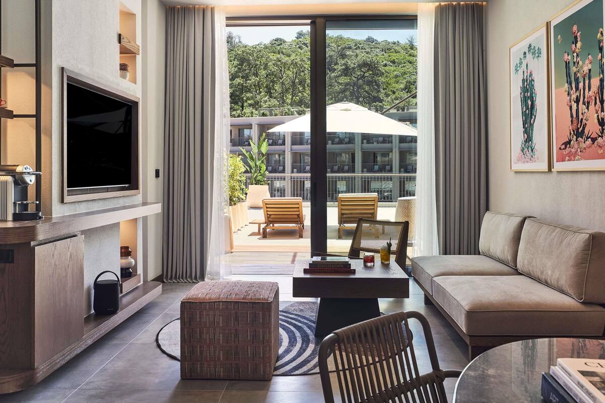 Uma sala de estar moderna com televisão de tela plana, um sofá, uma mesa de centro e vista para uma varanda com mobiliário externo.
