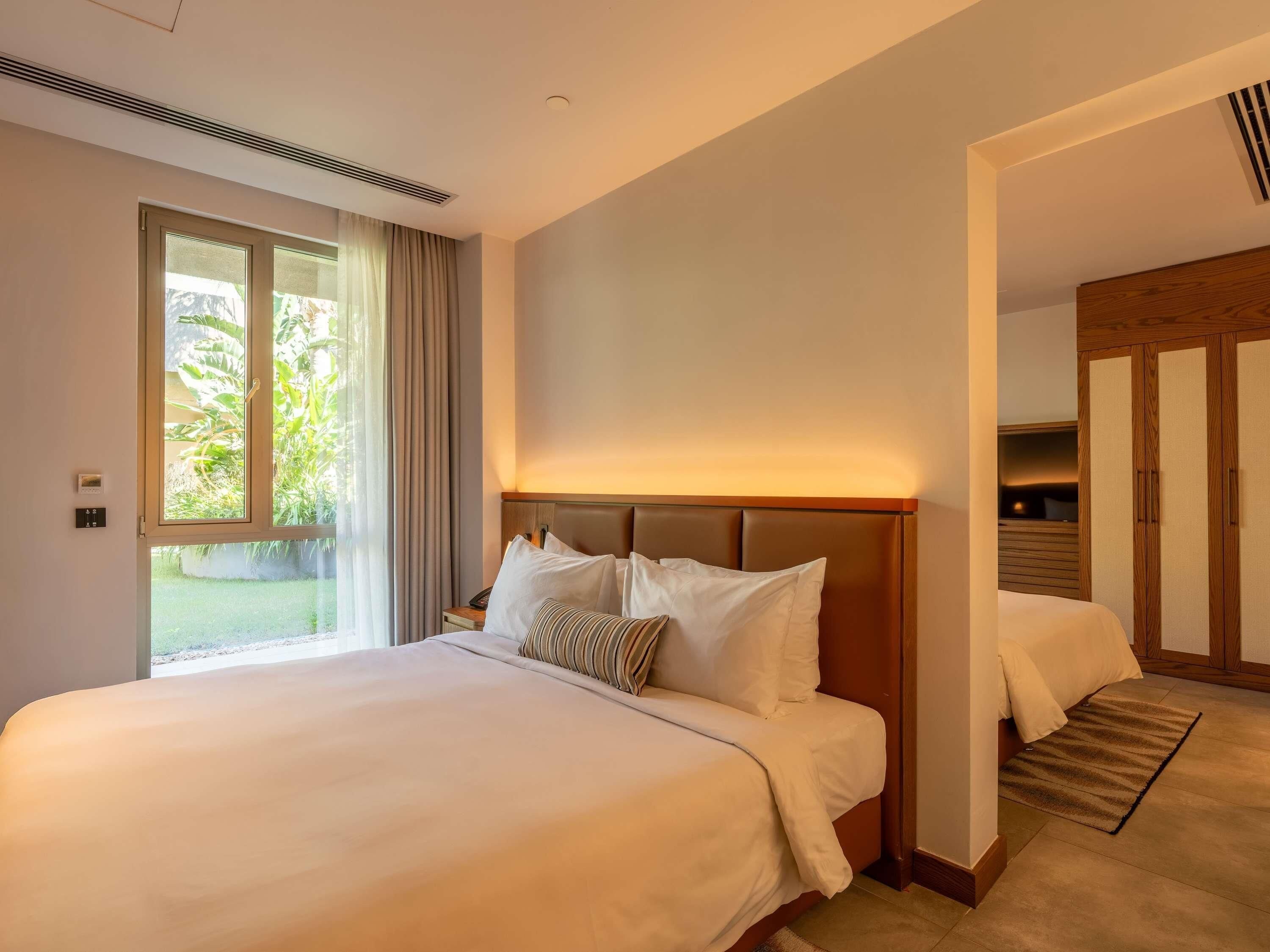 A hotel room with a large bed, a bedside table, a window with curtains, and a wardrobe.