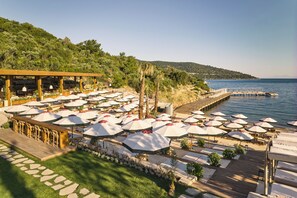 Un complejo turístico frente al mar con varias zonas de comedor al aire libre, una terraza de madera y un muelle que se adentra en el agua.