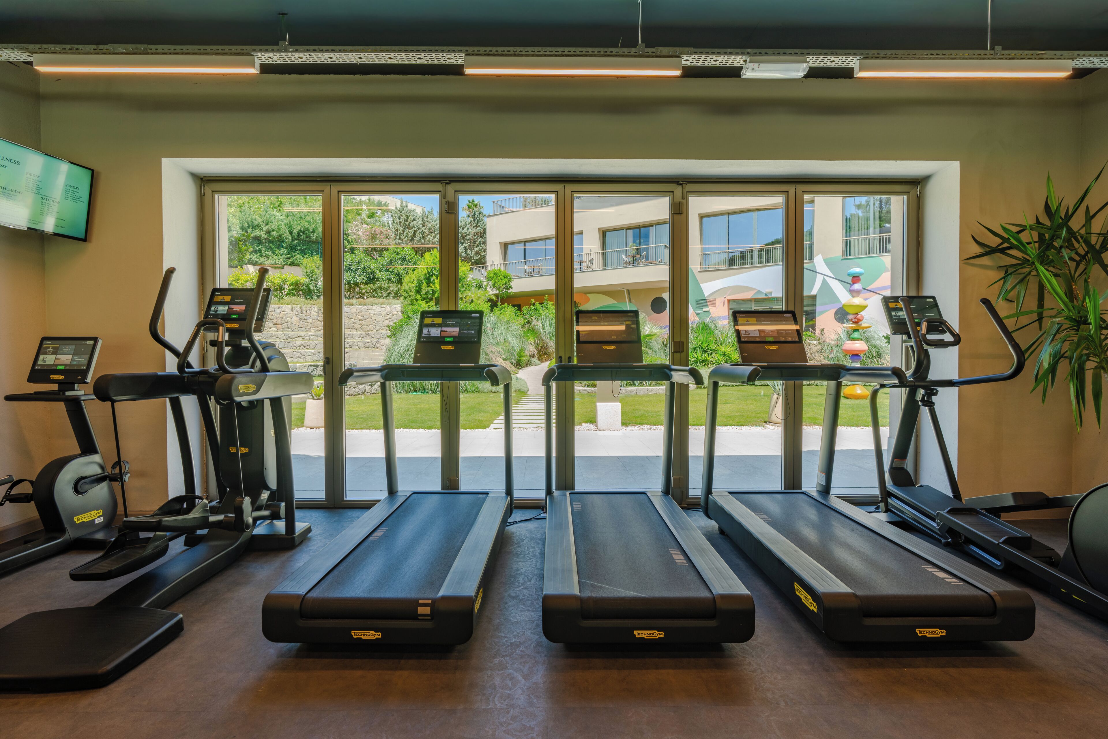 Ein Fitnessstudio mit Laufbändern, Crosstrainern und einem Fernsehbildschirm, der eine Speisekarte zeigt.