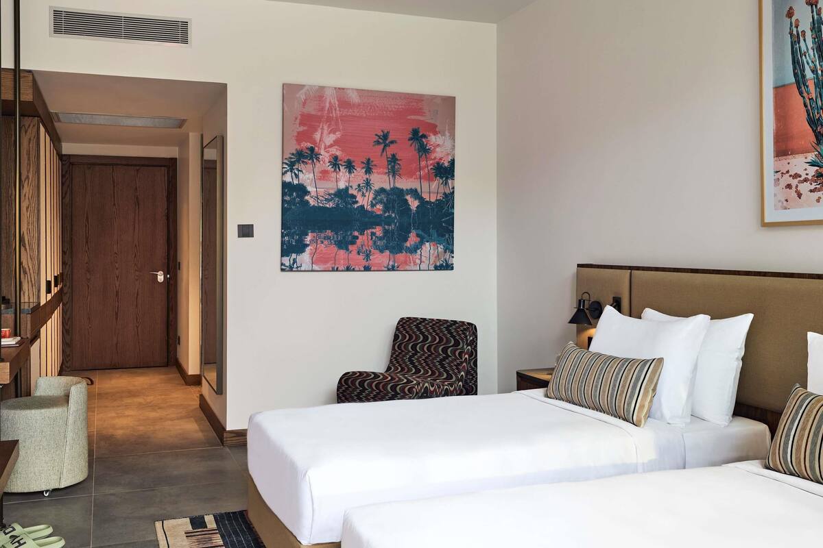 Quarto de hotel com cama, uma cadeira, mesa de cabeceira e um quadro na parede.