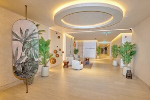 Un hall d’hôtel moderne doté d’un espace salon central, de plantes en pot et d’un plafond au design circulaire.